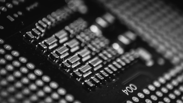 A close-up view of a computer motherboard with various electronic components, including chips and circuit traces. The image is in black and white, showing the intricate details and patterns of the hardware.