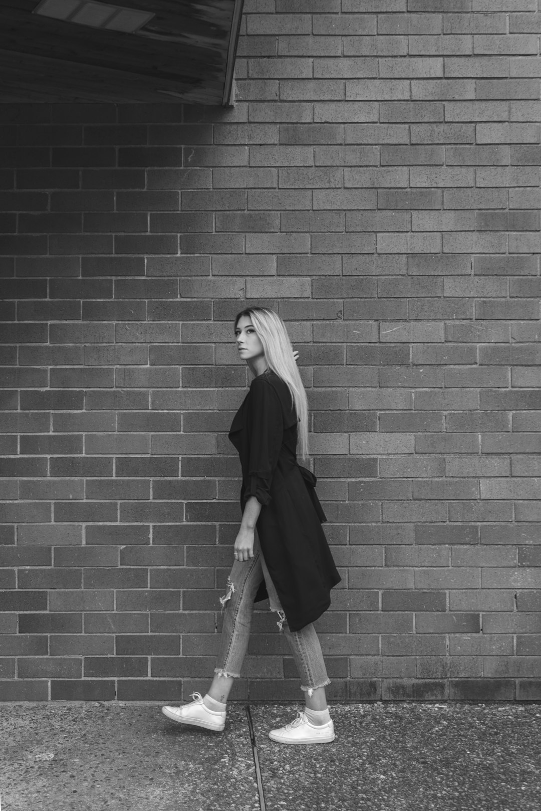 woman in black coat standing beside brick wall