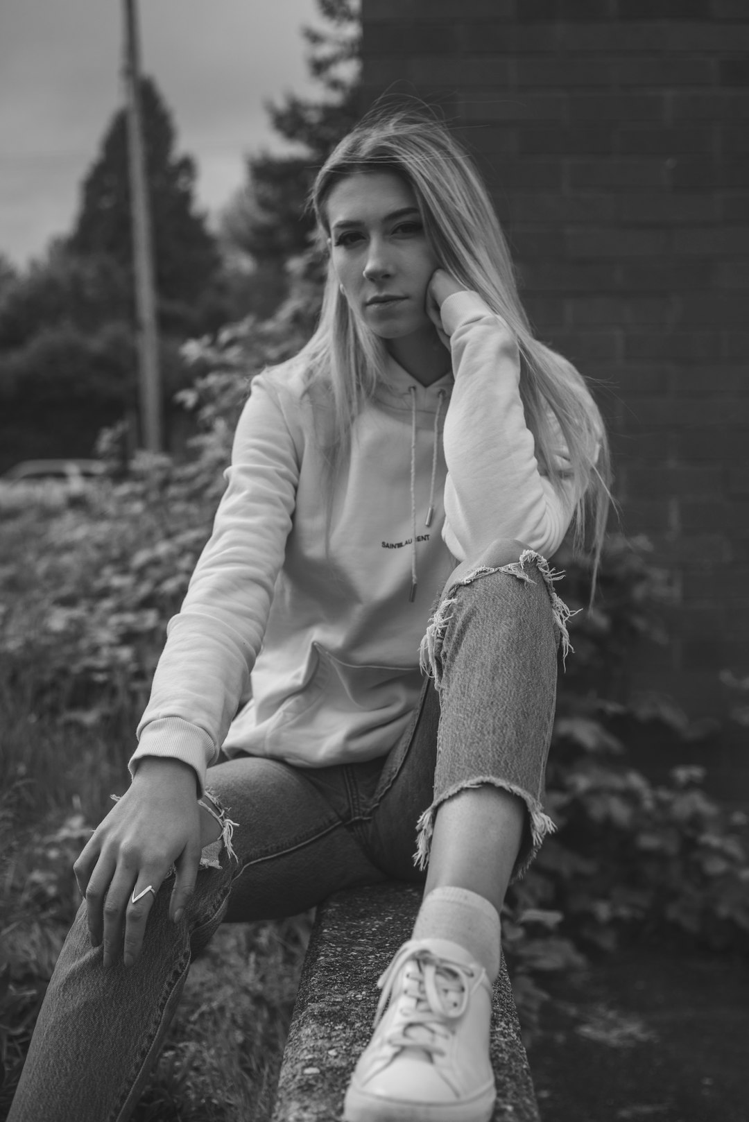 woman in white zip up jacket and gray denim jeans sitting on concrete wall