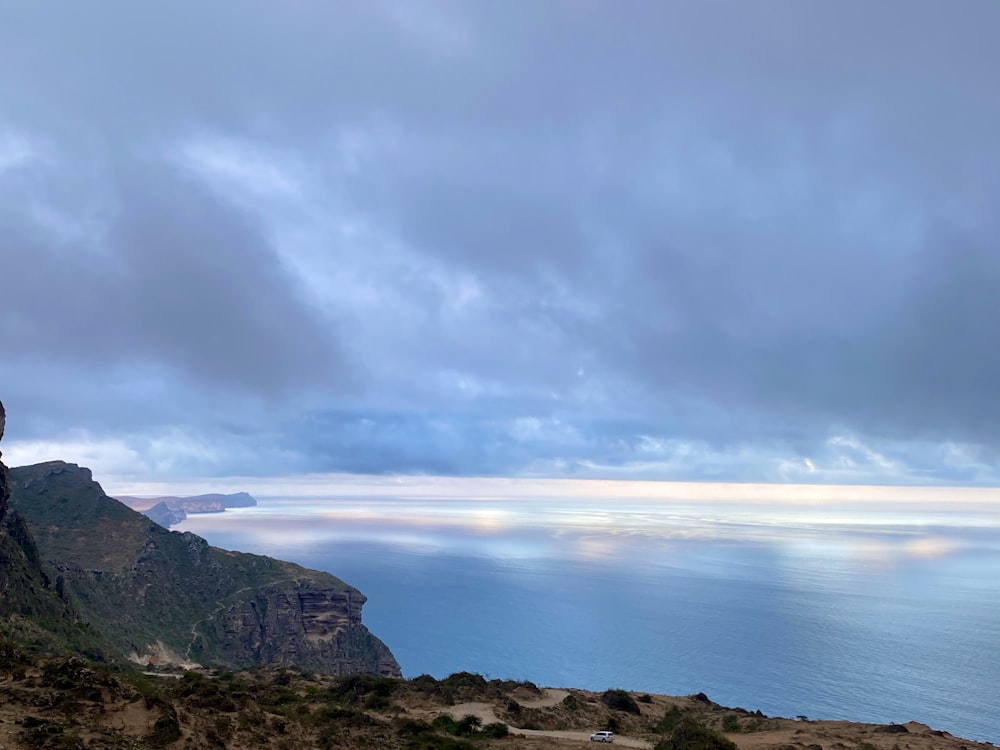 body of water near mountain under cloudy sky during daytime