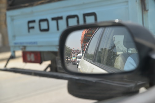 Close-up of a delivery truck's side mirror reflecting urban buildings.