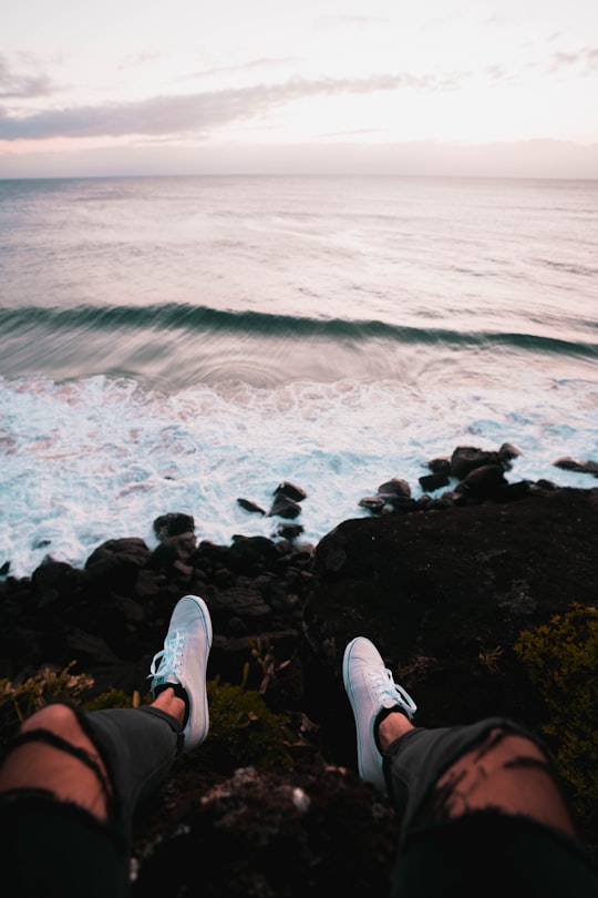 person in black shorts and white sneakers sitting on rock by the sea during daytime in Duranbah Beach Australia