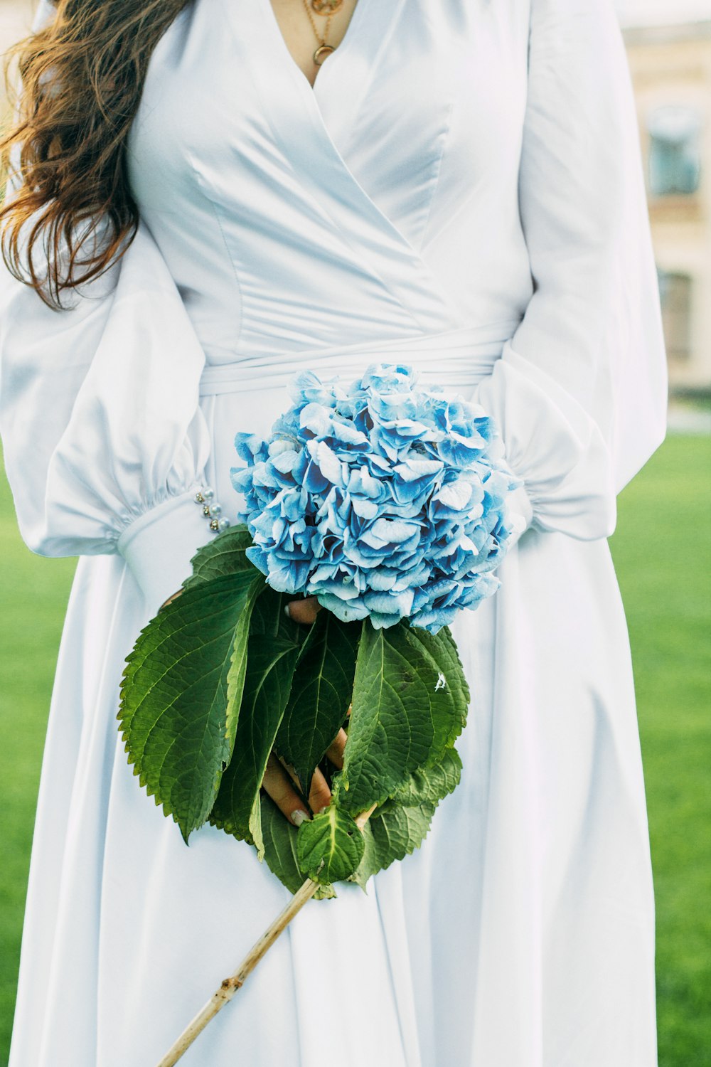 woman in white long sleeve dress holding blue flower bouquet