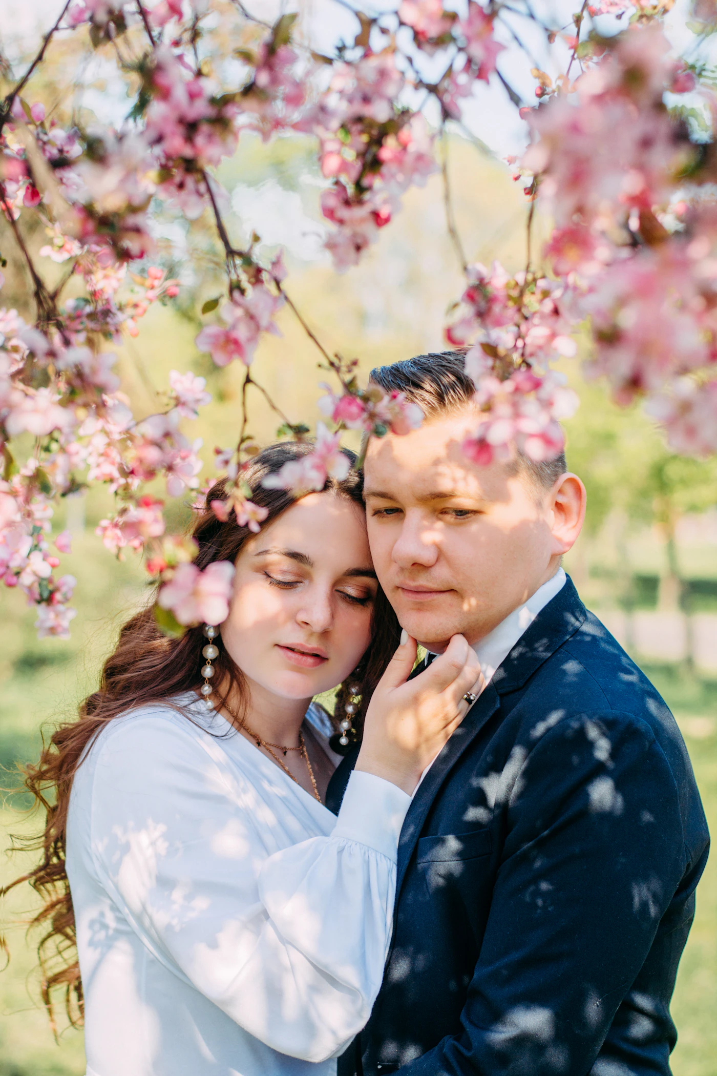 Couple in wedding attire sharing a kiss beneath a canopy of full blooming pink cherry blossom branches