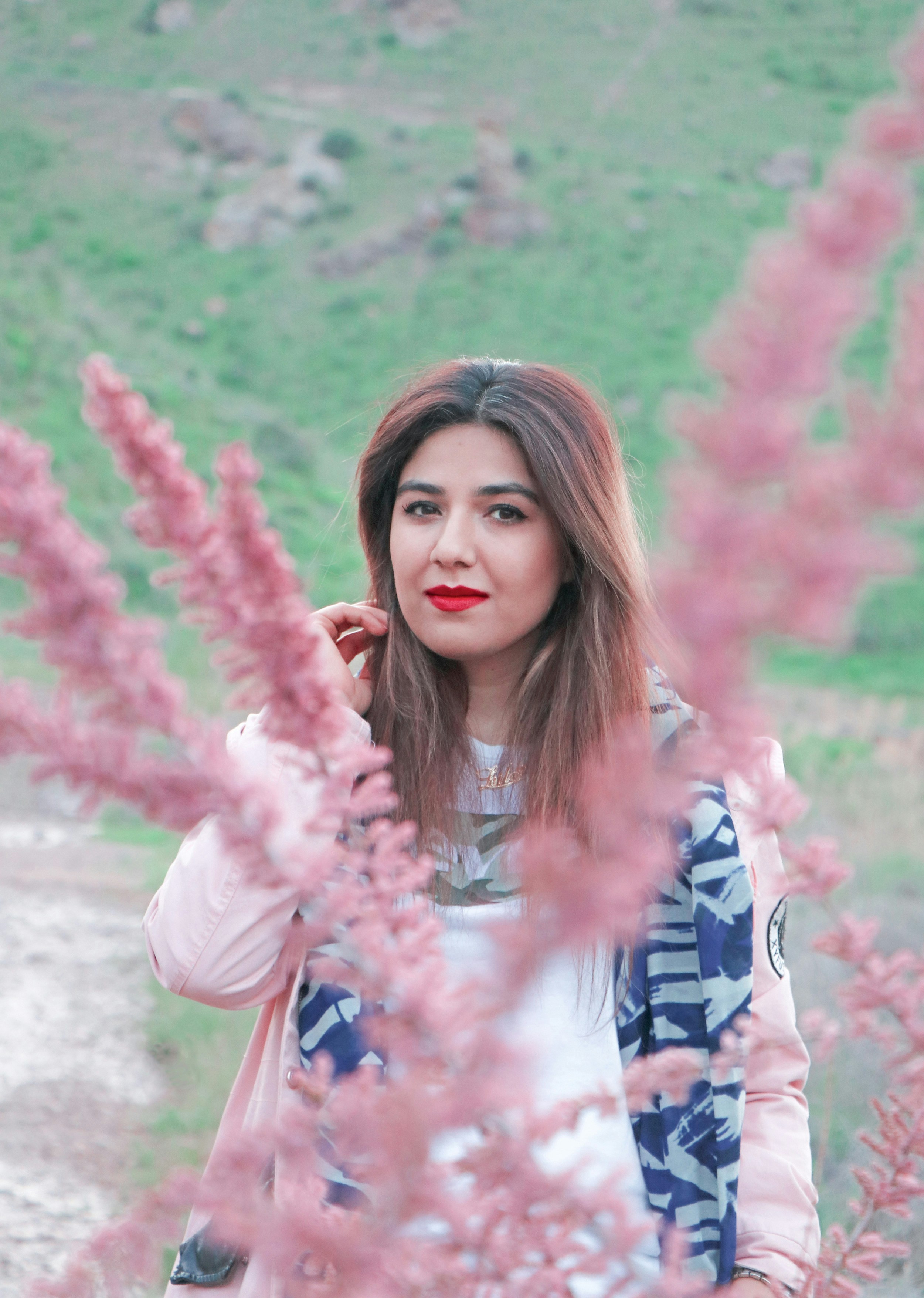 Gadis dengan jaket merah muda dan biru berdiri di atas pasir abu-abu di siang hari