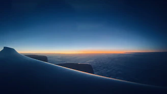 A close-up of an airplane wing cutting through clear blue skies at sunrise.