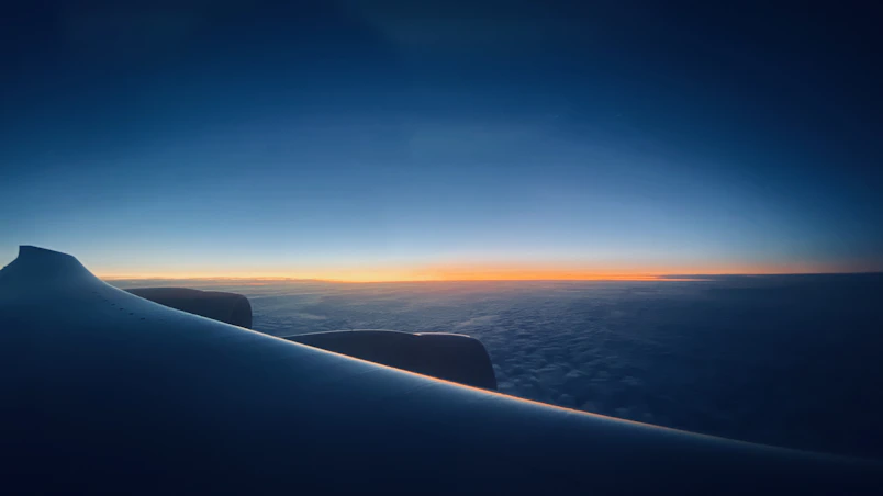 A close-up of an airplane wing cutting through clear blue skies at sunrise.