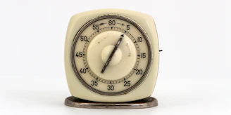 A vintage mechanical kitchen timer with a circular dial, marked with minute intervals from 0 to 60, is mounted on a small metal base.