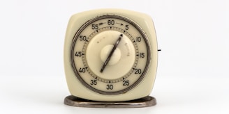 A vintage mechanical kitchen timer with a circular dial, marked with minute intervals from 0 to 60, is mounted on a small metal base.