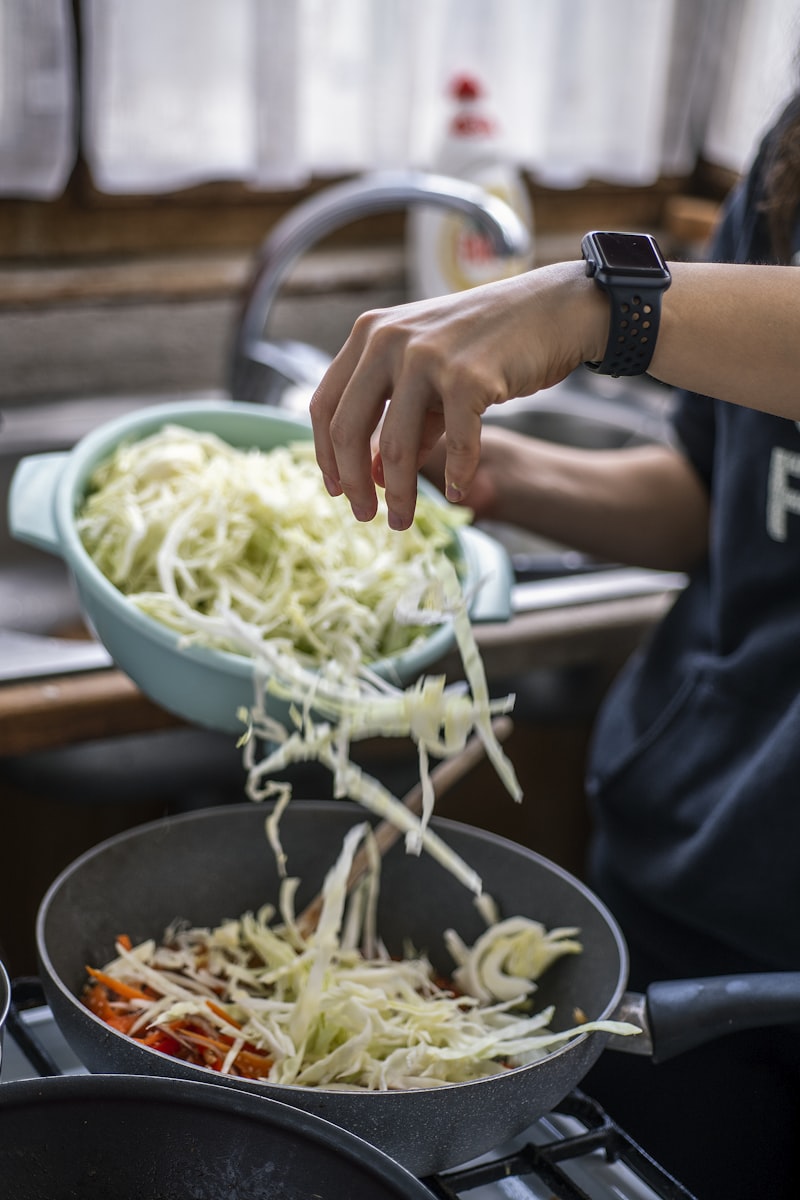 Shredded cabbage being added to a hot frying pan