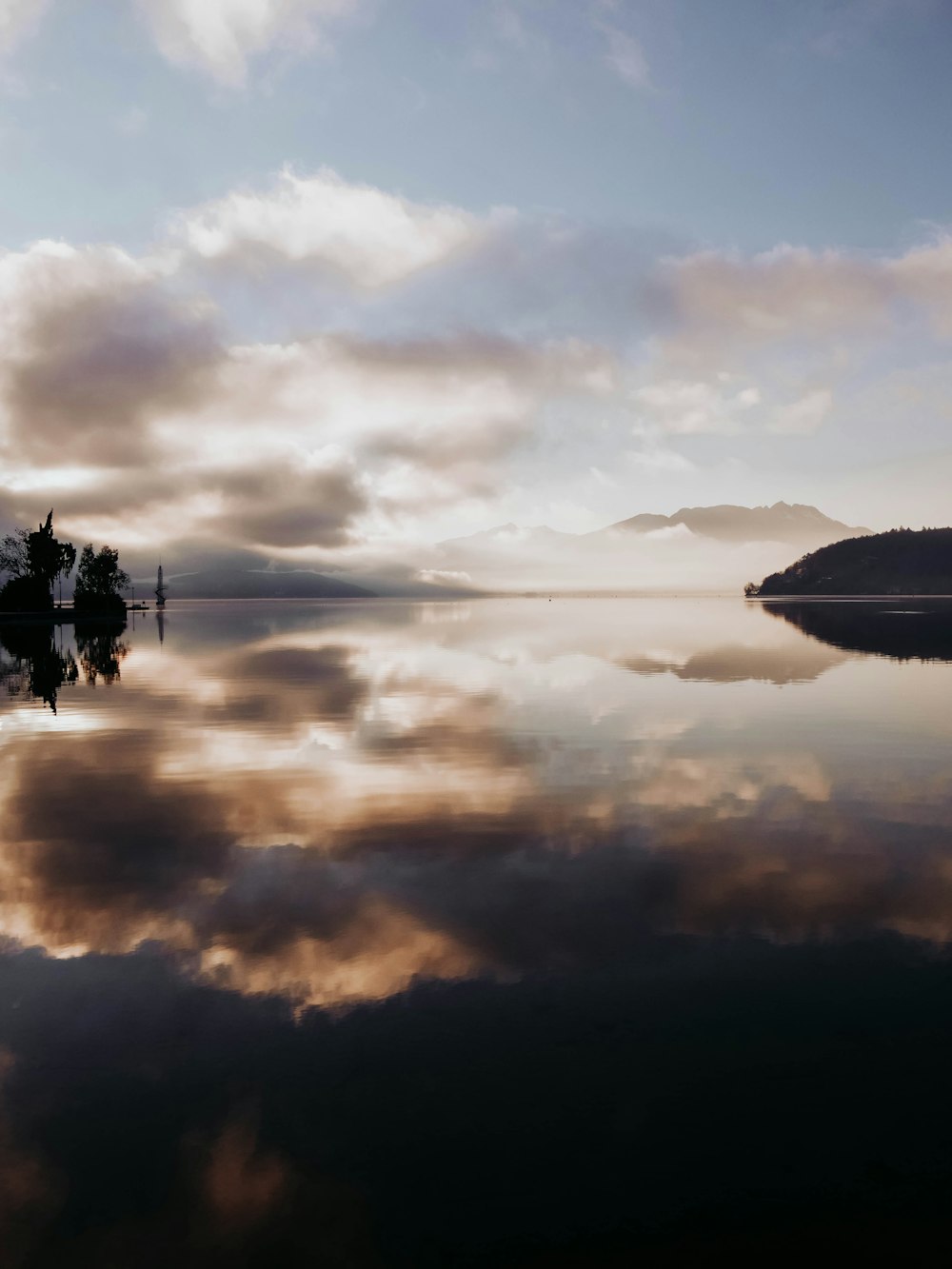 silhouette de bateau sur l’eau calme sous ciel nuageux pendant la journée