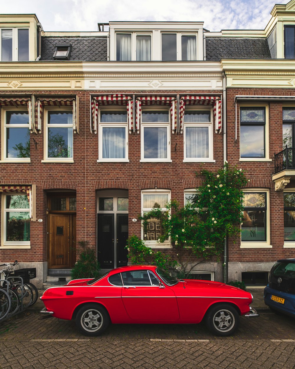 red coupe parked beside black motorcycle near brown concrete building during daytime