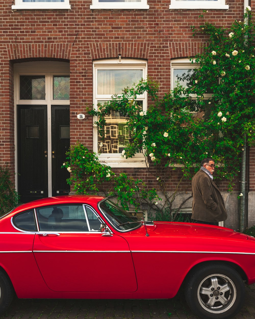 woman in brown coat standing beside red car during daytime