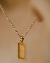 gold rectangular pendant necklace on white surface