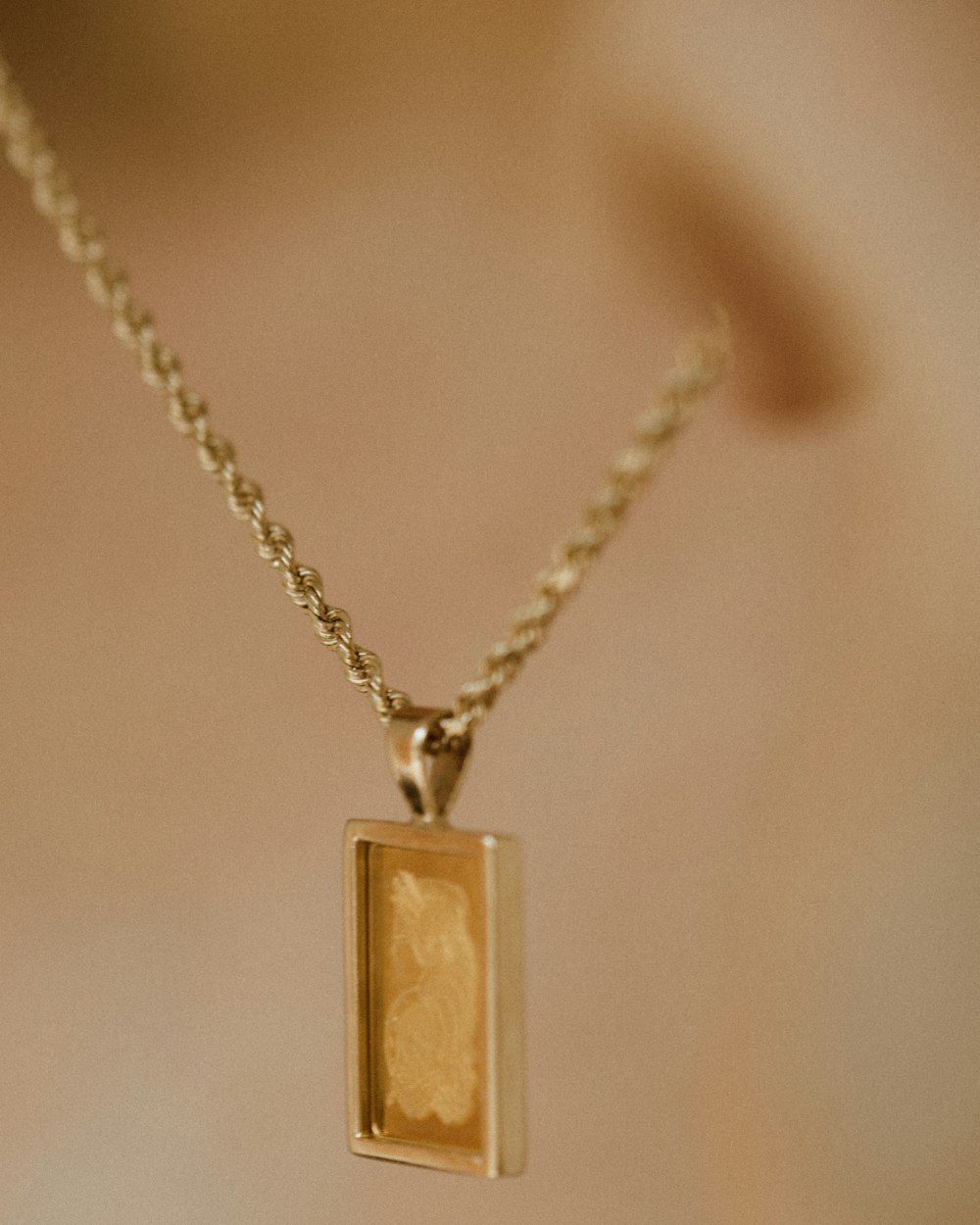gold rectangular pendant necklace on white surface