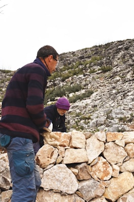 A team of contractors working together to build a stone retaining wall beside a fence.