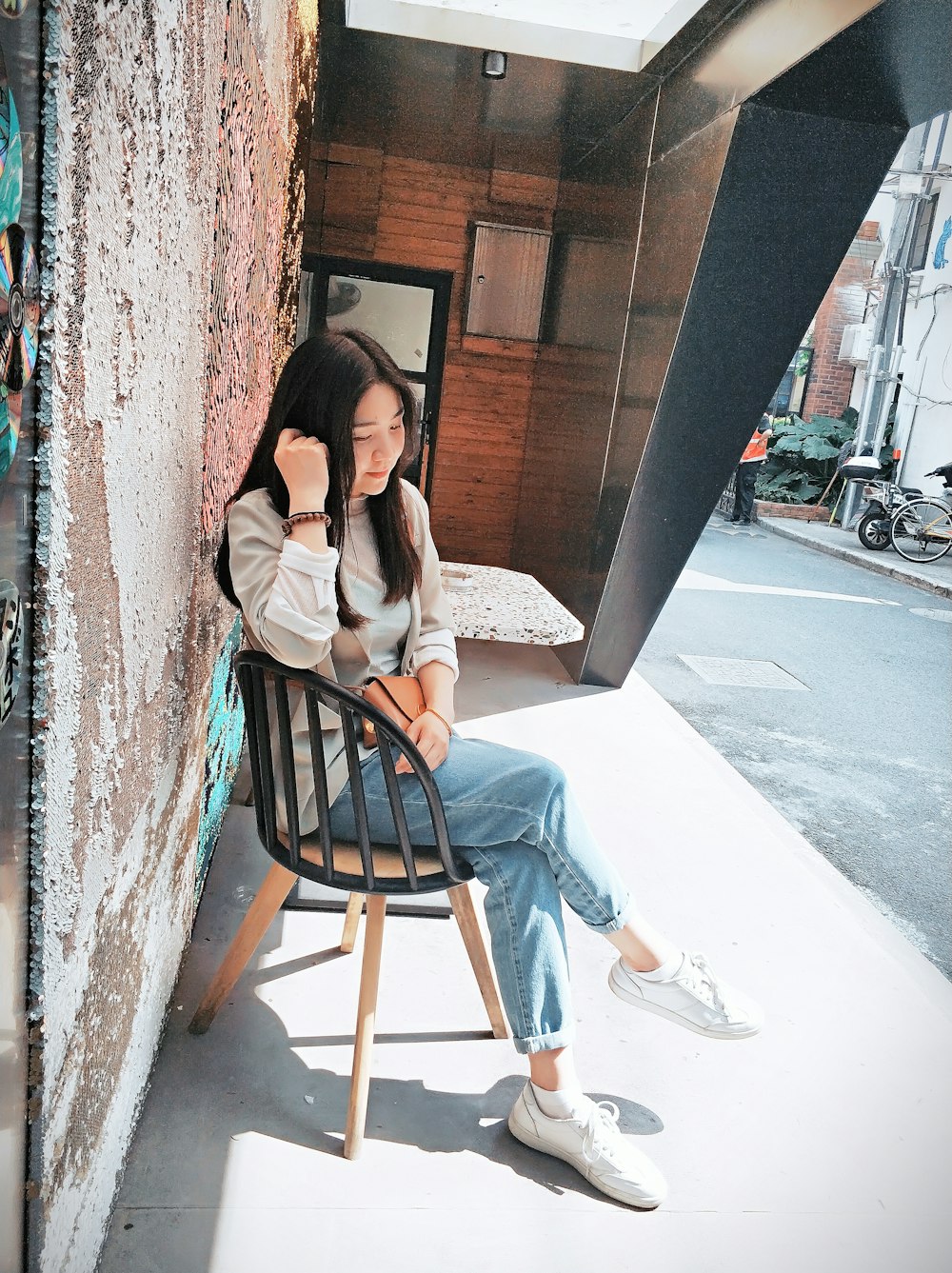 woman in pink long sleeve shirt and blue denim jeans sitting on brown wooden chair