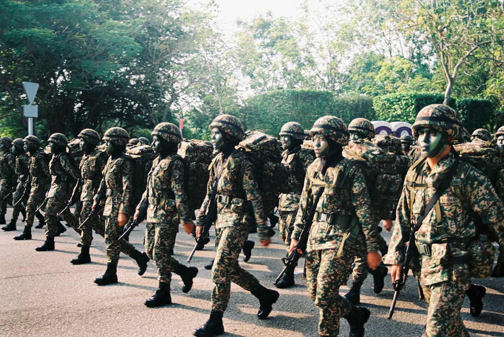 grupo de hombres con uniforme de camuflaje parados en la carretera durante el día