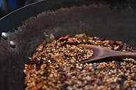 Hand gently sprinkling freshly ground spices into a sizzling pan.