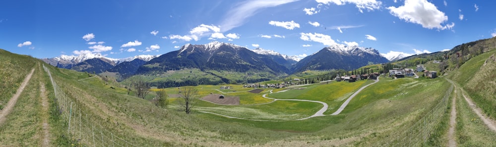 Grünes Grasfeld in der Nähe von Bergen unter blauem Himmel tagsüber