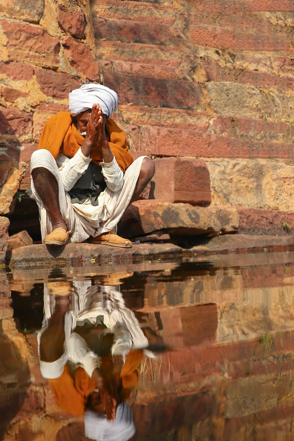 man in white thobe sitting on brown concrete wall