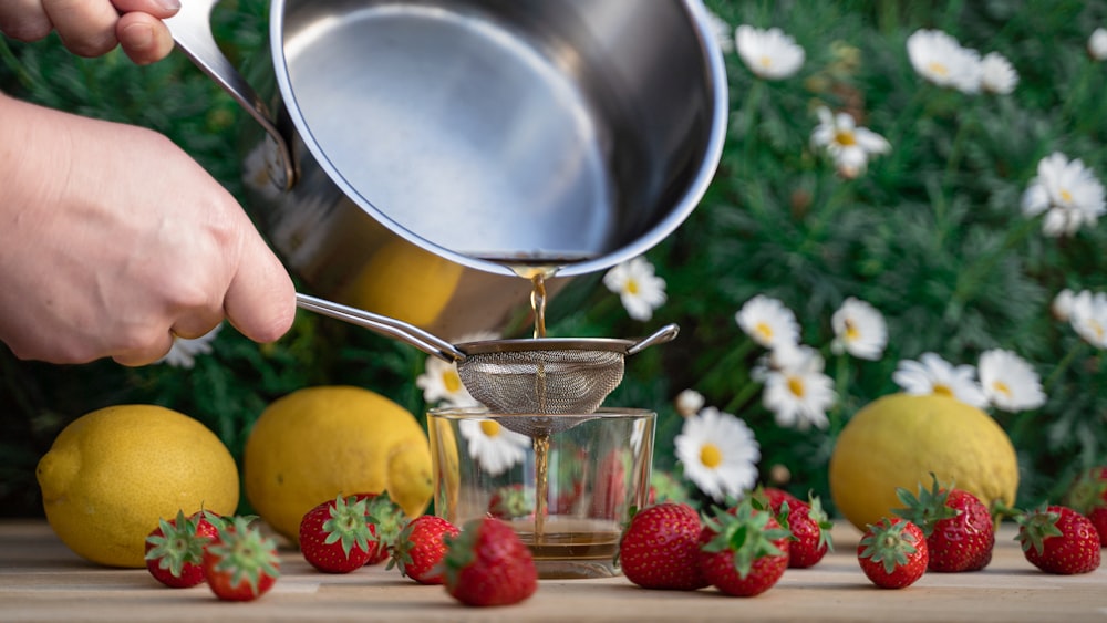 person pouring red strawberries on stainless steel bowl