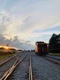 A rustic wooden caboose resting on old railroad tracks with a sunset backdrop.