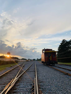 A rustic wooden caboose resting on old railroad tracks with a sunset backdrop.