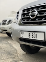 A close-up view of several parked Nissan cars, focusing on the front grille and license plate of the nearest vehicle, which has a Dubai registration number.