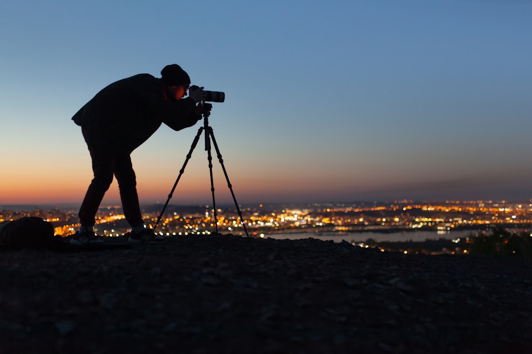 silhouette of man holding camera on tripod during sunset