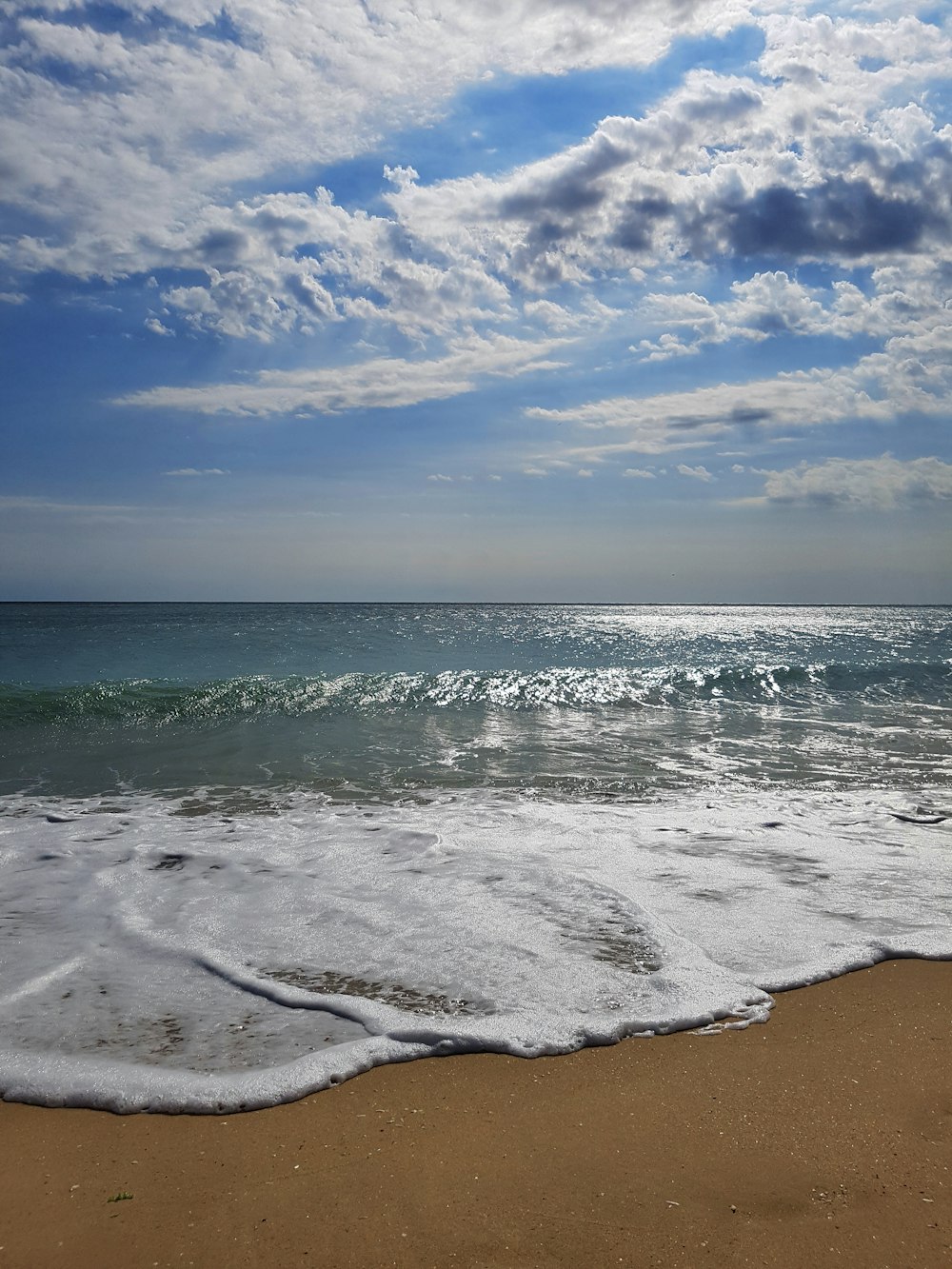 ondas do mar batendo na costa sob o céu azul e nuvens brancas durante o dia
