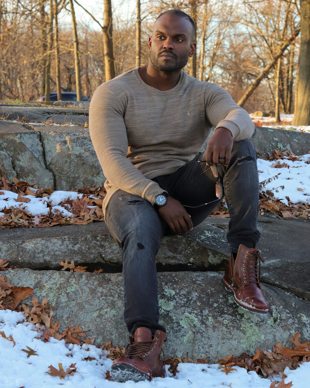 man in brown sweater and blue denim jeans sitting on brown concrete bench during daytime