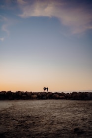 A small group gathered quietly on a rocky shore, watching the sun dip below the horizon.