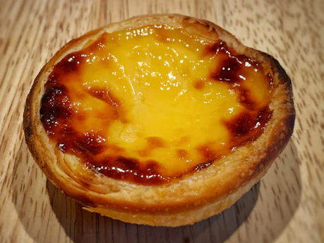 Close-up of a golden, freshly baked tart with a flaky crust and vibrant fruit topping on a rustic wooden table.