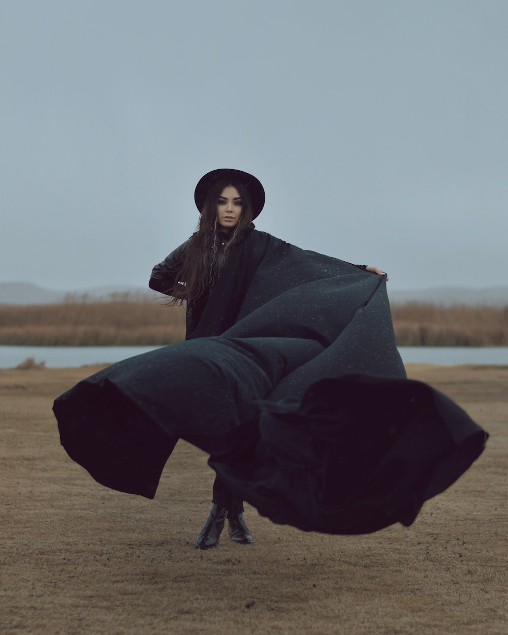 Frau in schwarzer Robe sitzt tagsüber auf braunem Feld