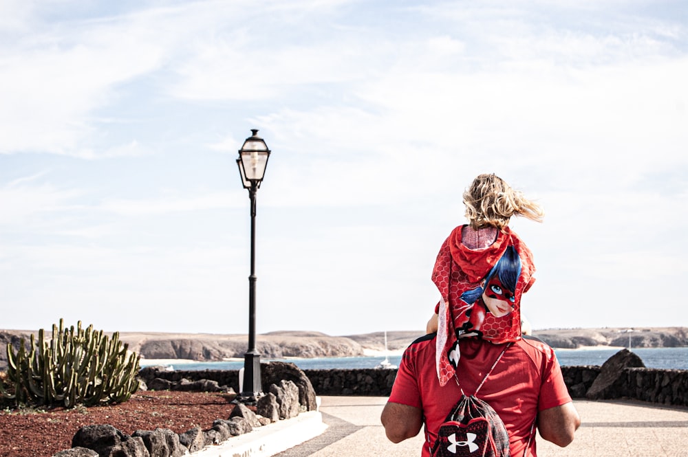 woman in red jacket and black pants sitting on concrete bench looking at the sea during