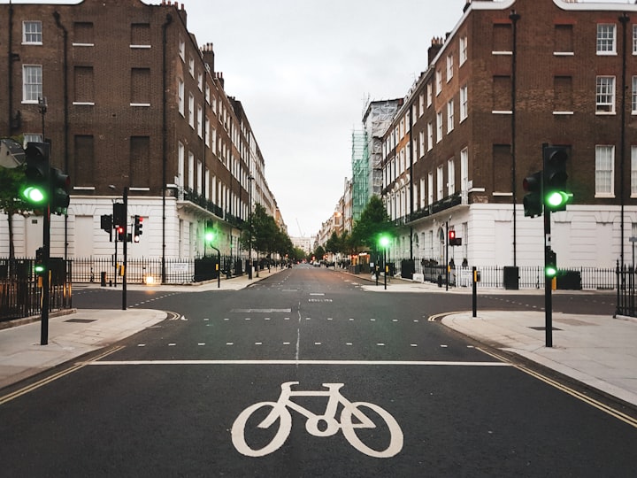 Photo of an empty street in London with green traffic lights around an intersection with crosswalks and bike path markings