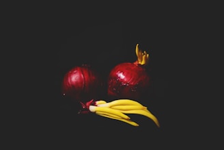Two red onions are placed against a dark background, enhanced by a dramatic spotlight effect. Yellow bean sprouts are emerging from the tops of the onions, adding a contrasting color and an interesting texture.