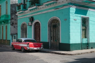 red coupe parked beside blue concrete building during daytime