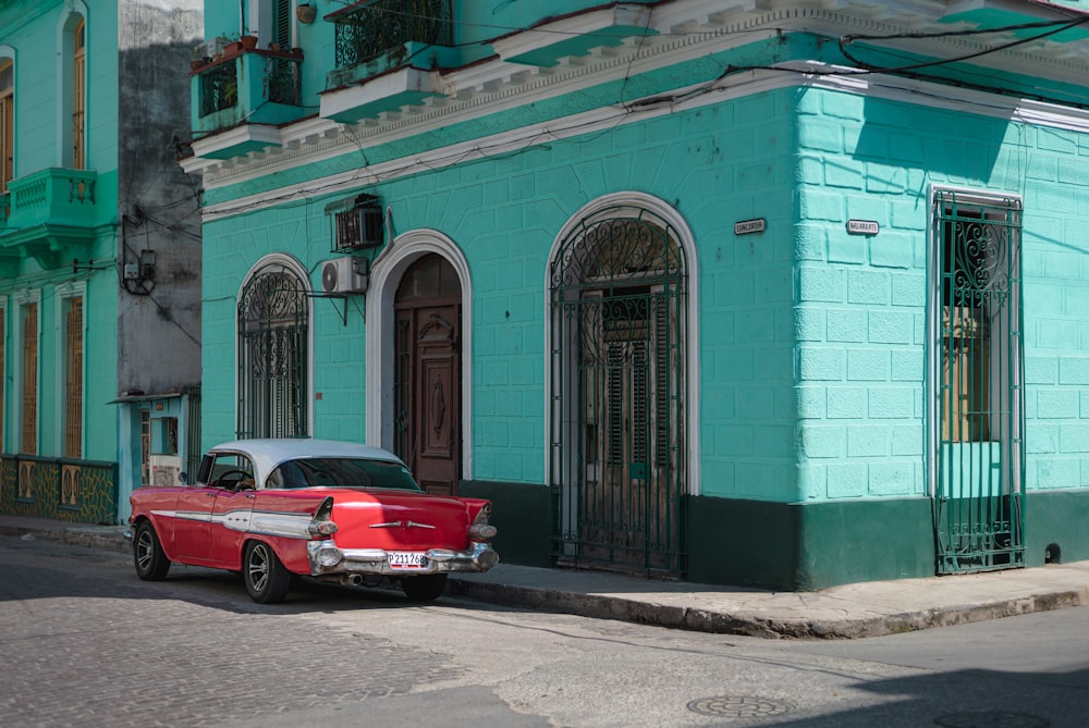 昼間、青いコンクリートの建物の脇に停車する赤いクーペ