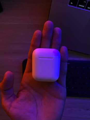 A sleek wireless earbud case glowing softly on a wooden desk with ambient RGB lighting in the background.