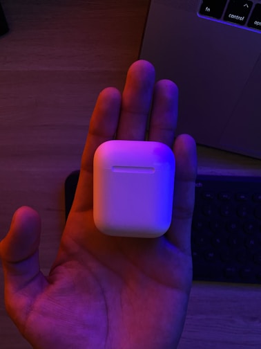 Hands holding a sleek wireless headset in a bright office environment.