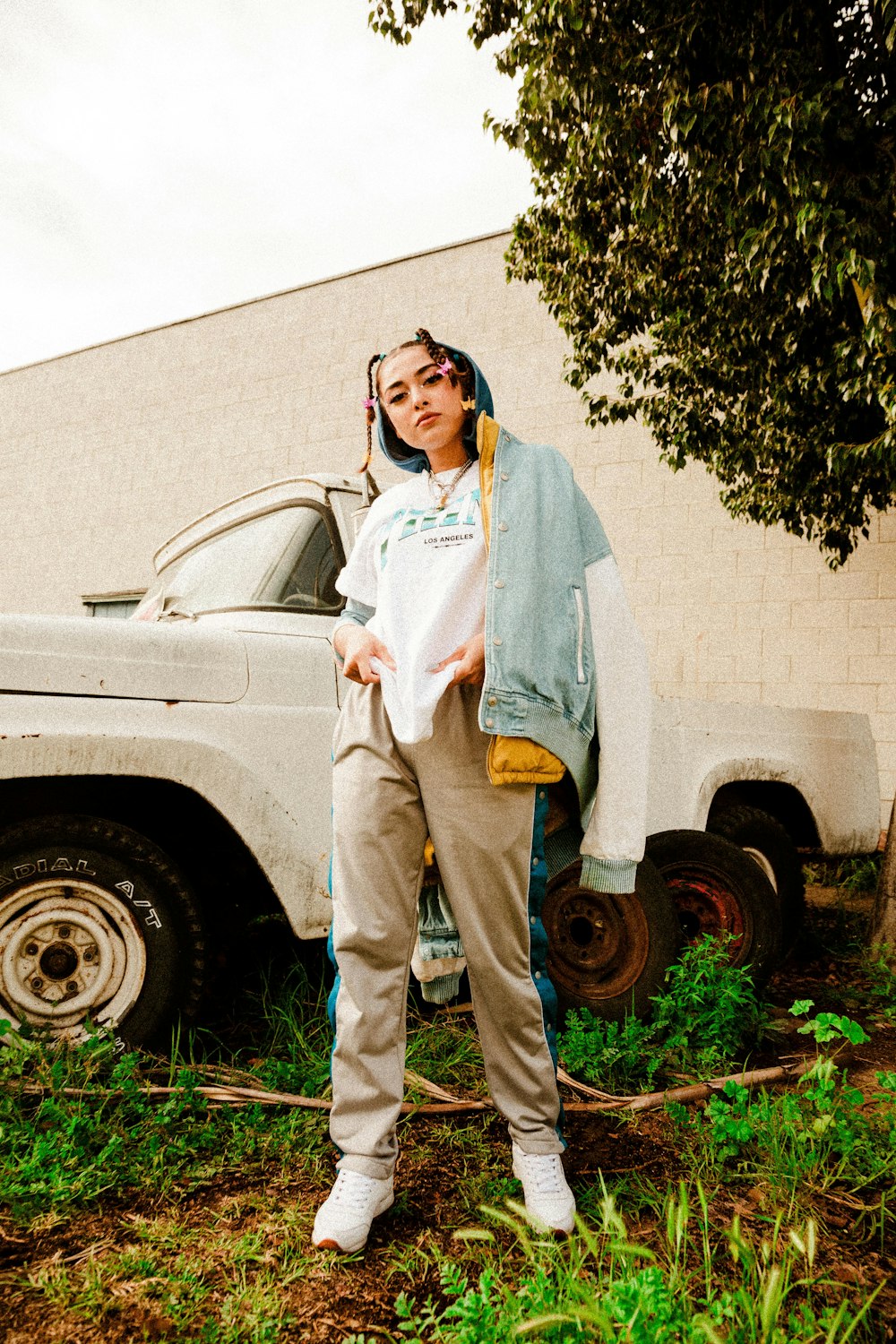 mulher na camisa azul de manga comprida e calças marrons de pé ao lado do carro branco