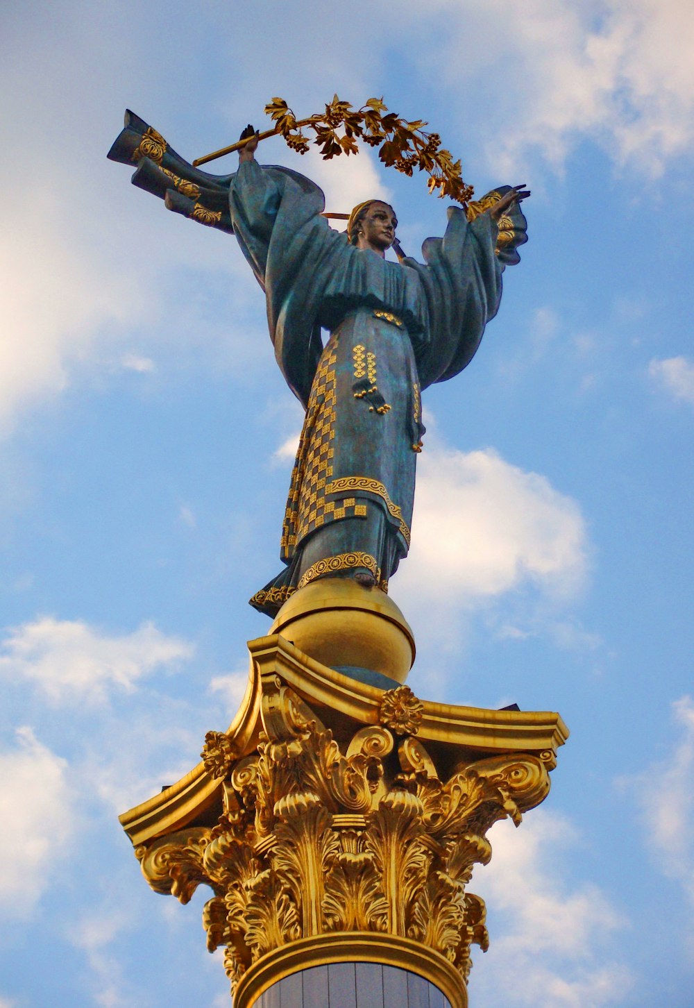 Goldene Statue eines Mannes, der tagsüber ein Buch unter blauem Himmel hält