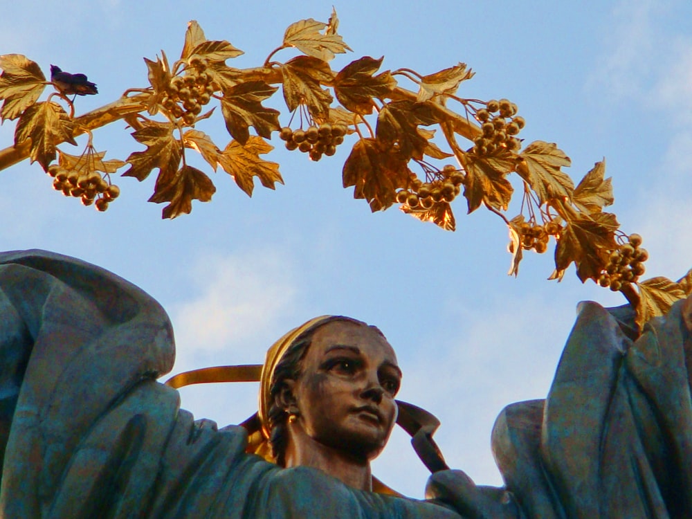 Photographie en contre-plongée de feuilles brunes sur la statue du visage de l’homme sous le ciel bleu pendant la journée