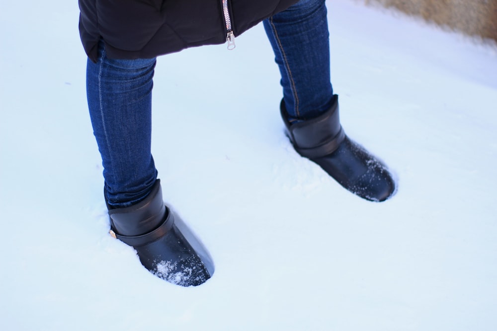 person in black leather boots and blue denim jeans walking on snow covered ground during daytime