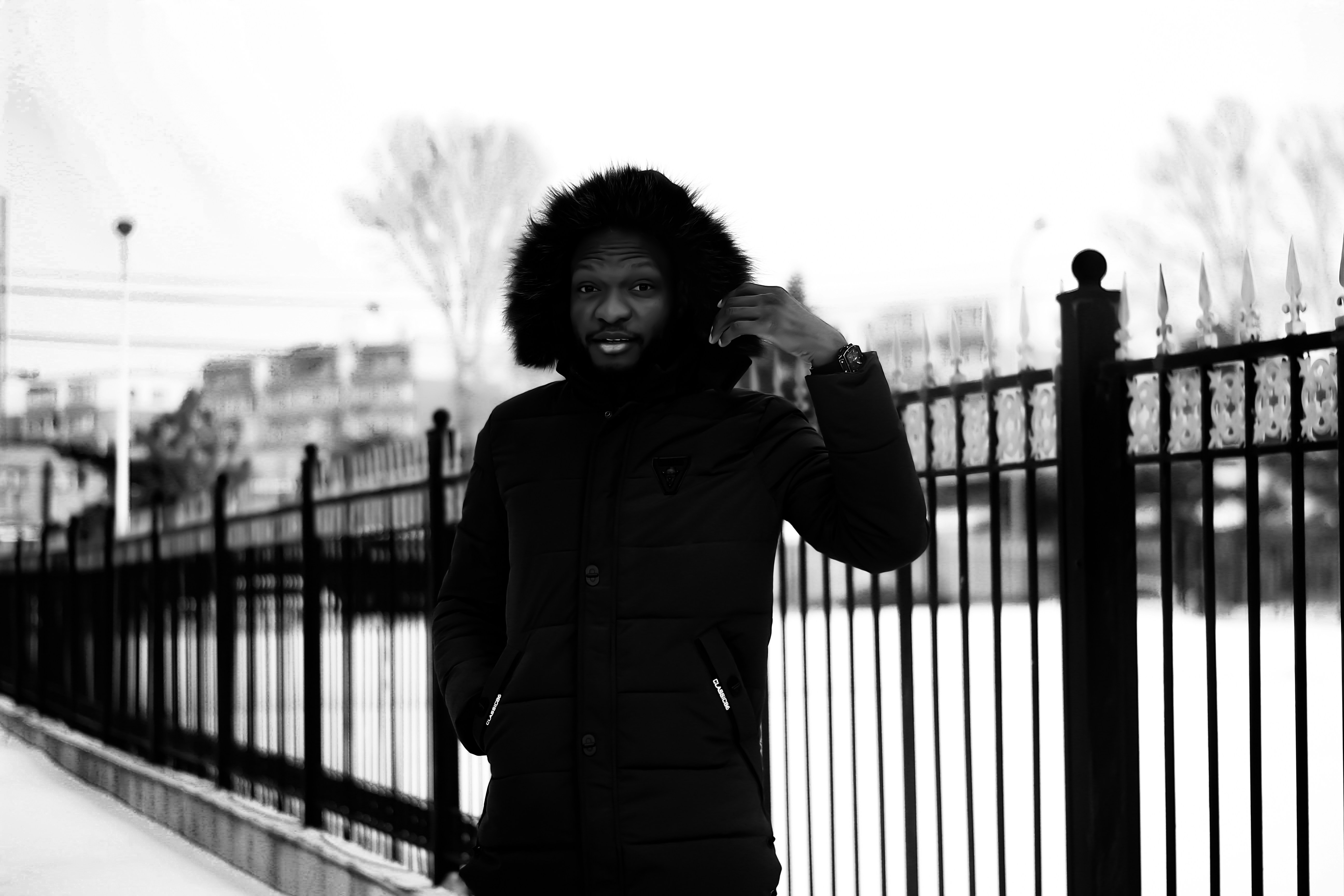 昼間、黒い金属製の柵のそばに立つ黒いジャケットを着た女性