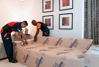 Professional movers carefully packing furniture with protective materials inside a modern home.