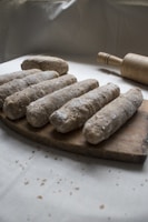 Several pieces of dough covered with flour are arranged on a wooden cutting board. A rolling pin is placed nearby. The setting suggests preparation for baking, with a rustic, homemade feel.