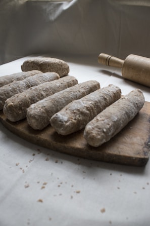 Several pieces of dough covered with flour are arranged on a wooden cutting board. A rolling pin is placed nearby. The setting suggests preparation for baking, with a rustic, homemade feel.
